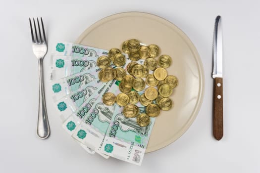 On the plate is a bunch of Russian ten-thousandths of bills and coins lay near cutlery, top view