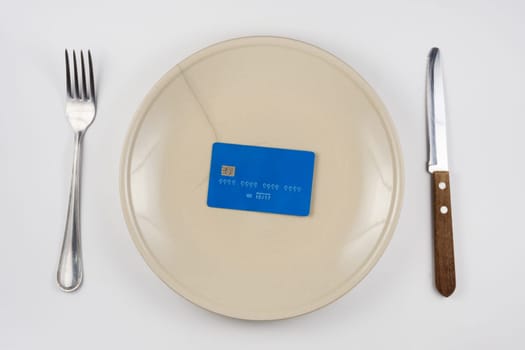 On the cracked plate is a plastic credit card, next lie fork and knife, white background, top view