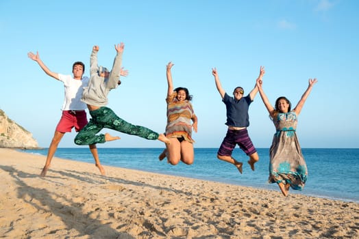 Group of happy teenage friends jumping at the beach