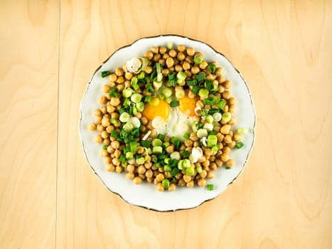 Plate with chick peas, fried eggs, chopped fresh onion with hands holding fork and knife, healthy eating, simple top view, copy space