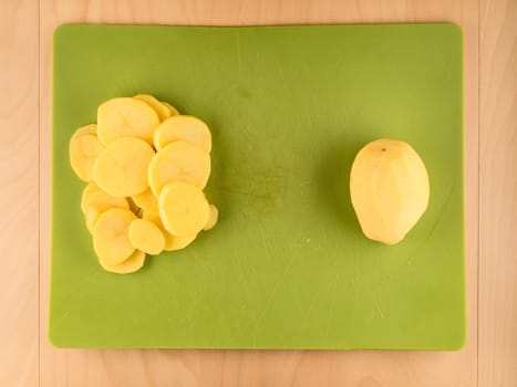 Pattern of sliced peeled potatoes on green used plastic board, simple food preparation illustration, vegetarian dieting, still life with center composition, close up