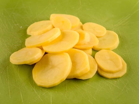 Pattern of sliced peeled potatoes on green used plastic board, simple food preparation illustration, vegetarian dieting, still life with center composition, close up