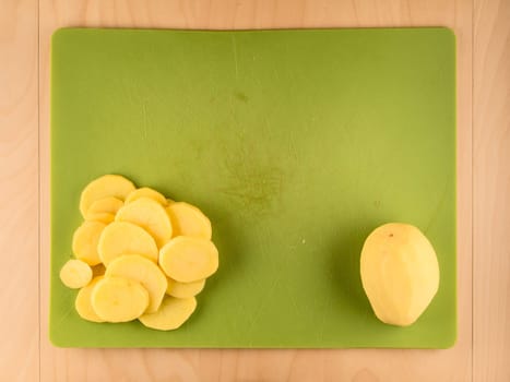 Pattern of sliced peeled potatoes on green used plastic board, simple food preparation illustration, vegetarian dieting, still life with center composition, close up