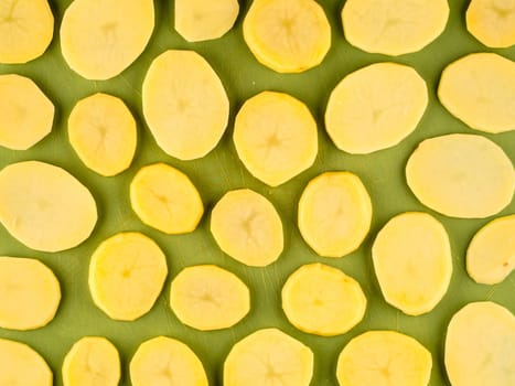 Pattern of sliced peeled potatoes on green used plastic board, simple food preparation illustration, vegetarian dieting, still life with center composition, close up