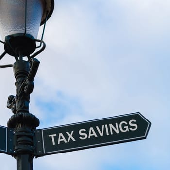 Street lighting pole with conceptual message TAX SAVINGS on directional arrow over blue cloudy background.