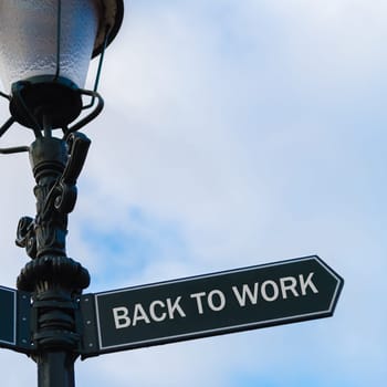 Street lighting pole with conceptual message BACK TO WORK on directional arrow over blue cloudy background.