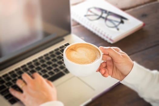 Hand on cup of coffee at work table, stock photo