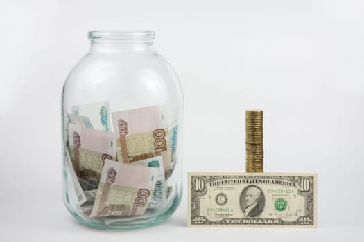 Close to three-liter jar filled with money is a stack of coins next to it is a banknote of ten dollars