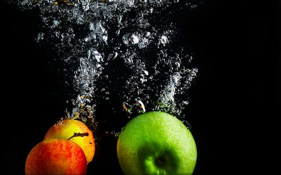 Apples falling into the water with a splash and air bubbles. Healthy food on black background. Wash fruits.