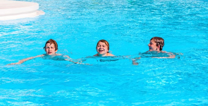 three friends swimming in a row in the pool