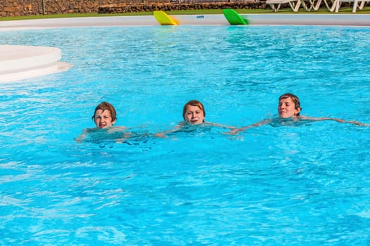 three friends swimming in a row in the pool