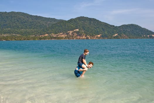 brothers are jumping and playing on a idyllic beach and having fun in the water