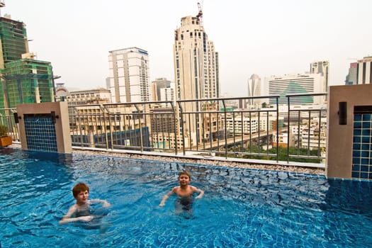boys are swimming in an open air pool with beautiful view to the skyscrapers