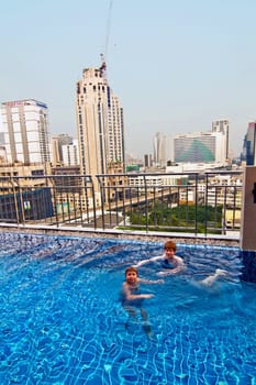 boys are swimming in an open air pool with beautiful view to the skyscrapers