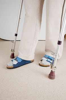 Lower leg view of an elderly woman standing on crutches in the living room at home after a hip operation.