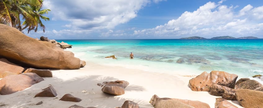 Active sporty man wearing black swimsuit enjoying swimming and snorkeling at amazing on Anse Patates beach on La Digue Island, Seychelles. Summer vacations on picture perfect tropical beach concept.