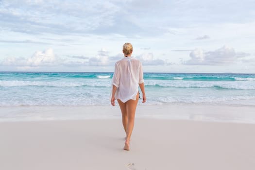 Woman wearing white loose tunic over bikini on Mahe Island, Seychelles. Summer vacations on picture perfect tropical beach concept.