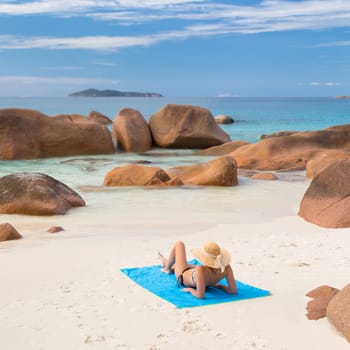 Woman wearing black bikini and beach hat, sunbathing at Anse Lazio beach on Praslin Island, Seychelles. Summer vacations on picture perfect tropical beach concept.
