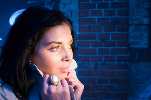 Young black-haired woman on a brick wall sprayed with graffiti illuminated with artificial light in the evening.