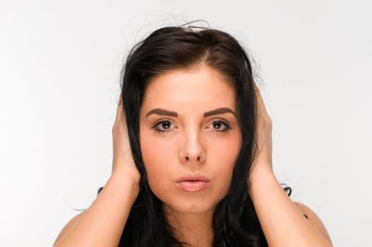 Frontal head portrait of a young black-haired woman holding her ears against a white background.