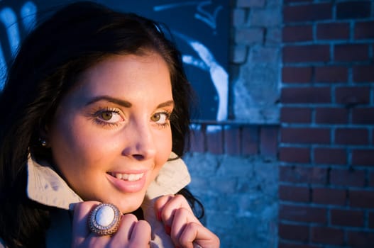 Young black-haired woman on a brick wall sprayed with graffiti illuminated with artificial light in the evening.