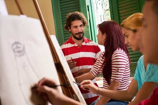 School of art, college of arts, education for group of young students. Professor helping student, man at work as teacher giving class of charcoal painting.