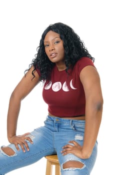 A pretty African American woman in ripped jeans and burgundy top.sitting on a chair, isolated for white background..
