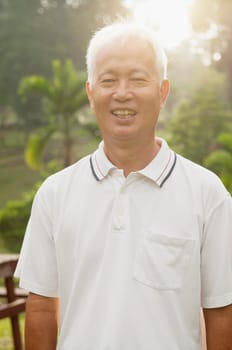 Portrait of healthy Asian senior man smiling at outdoor nature park, morning beautiful sunlight background.