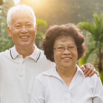 Portrait of healthy Asian seniors retiree couple relaxing at outdoor nature park, morning beautiful sunlight background.