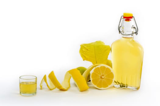 Open glass decanter bottle and shot glass filled with yellow lemon liquor or limoncello or limoncino on white. Peeled natural organic lemon.