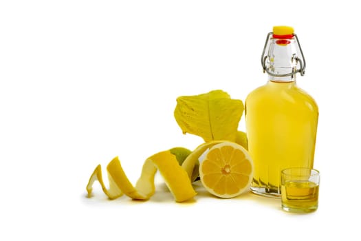 Open glass decanter bottle and shot glass filled with yellow lemon liquor or limoncello or limoncino on white. Peeled natural organic lemon.