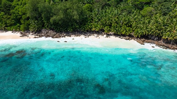 Waves gently wash over the white sand beach surrounded by tropical vegetation. Anse Intendance. Seychelles, Mahe.