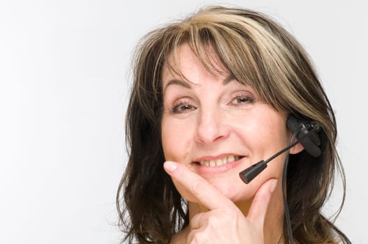 Frontal head portrait of a middle-aged woman with headphone set against a white background thumb and index finger touching the chin.