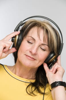 Head-and-shoulder view of a middle-aged woman with closed eyes and headphones against a white background.