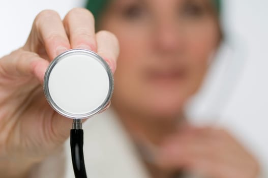 Doctor in the blurred background holds the membrane of a stethoscope in the direction of the camera
