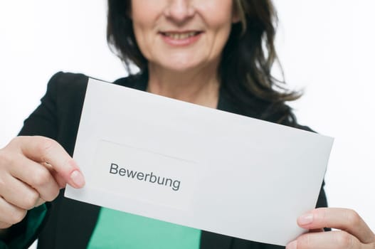 Upper body view of a middle-aged woman in the blurred background holds an envelope into the camera