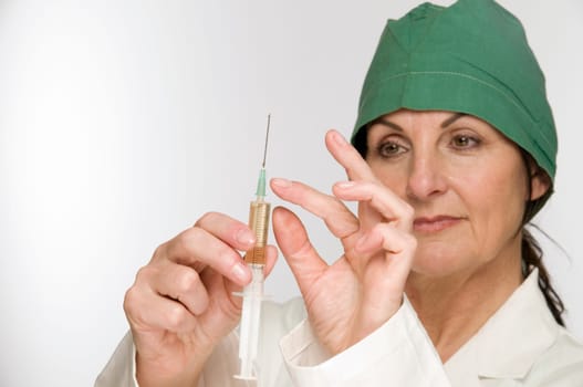 Head-and-shoulder view of a middle-aged woman with a green surgical hood against a white background holds a filled syringe in front of her.