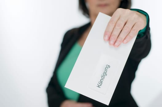 Upper body view of a middle-aged woman in the blurred background holds an envelope into the camera