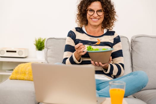 Beautiful woman at home sitting on the sofa working and eating a apple