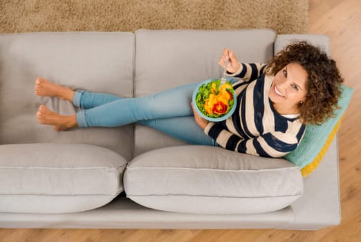 Top view of a beautiful woman on the sofa eating a healthy salade