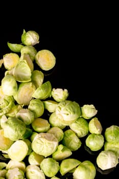 green fresh whole and cut organic Brussels sprouts, isolated on black glossy background