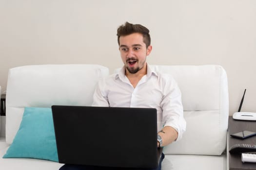 Surprised shocked man with opened mouth work at home with laptop
