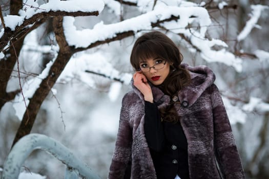 Student with glasses and fur coat in the winter forest with white snow, red lips.Beautiful teacher, student with glasses, fur coat in winter forest.