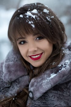 Close-up portrait of very beautiful,cute,cheerful,smiling girl with nice,healthy smile,white teeth,dentist,red lips,attractive face,brown eyes,fashionable,glamorous,cheekbone,white snow in the long,brunette,curly hair.Nice smile.Cute smile.Winter,sex