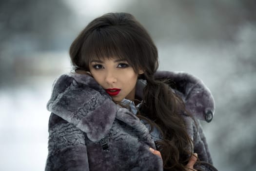 Rich,fashionable,glamorous model,girl with gorgeous mouton grey fur coat and red leps. Very beautiful portrait of attarctive girl.Fashionable,glamorous model,girl with gorgeous mouton grey fur coat.Close-up portrait of stunning girl with perfect face
