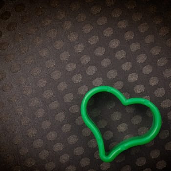Green plastic heart shape on a dark background with space for text