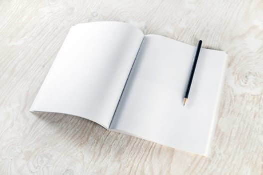 Blank opened brochure with a pencil on light wooden table background. Mockup for placing your design. Top view.
