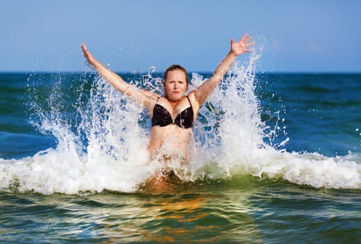 Beautiful girl on a background of blue sea with waves and clear sky on a sunny day. Sexy woman in bikini enjoying a dip in the sea wave.