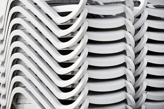 Folded stack of white plastic deck chairs. Pile of beach loungers. Abstract background or texture