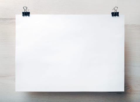 Blank white paper poster hanging on light wooden background. Blank template for placing your design. Front view.
